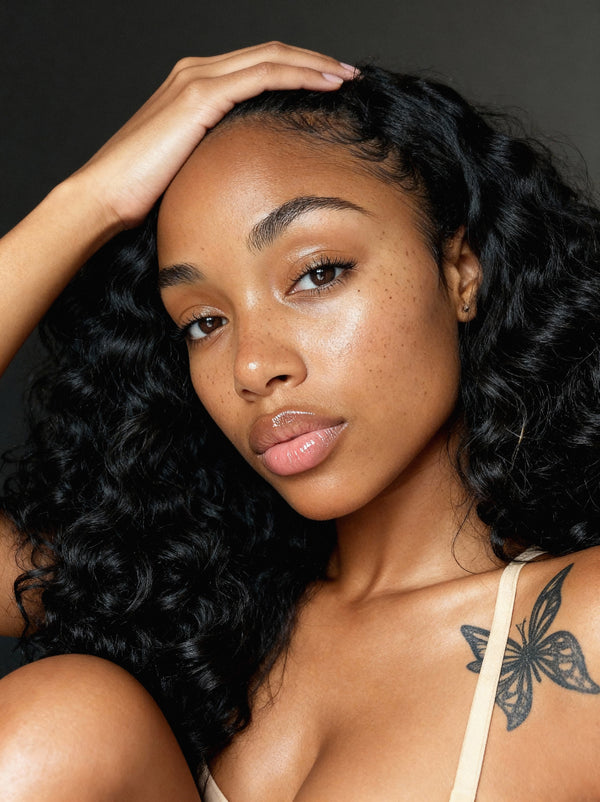 Woman with styled raw cambodian hair and a tattoo on her shoulder against a dark background