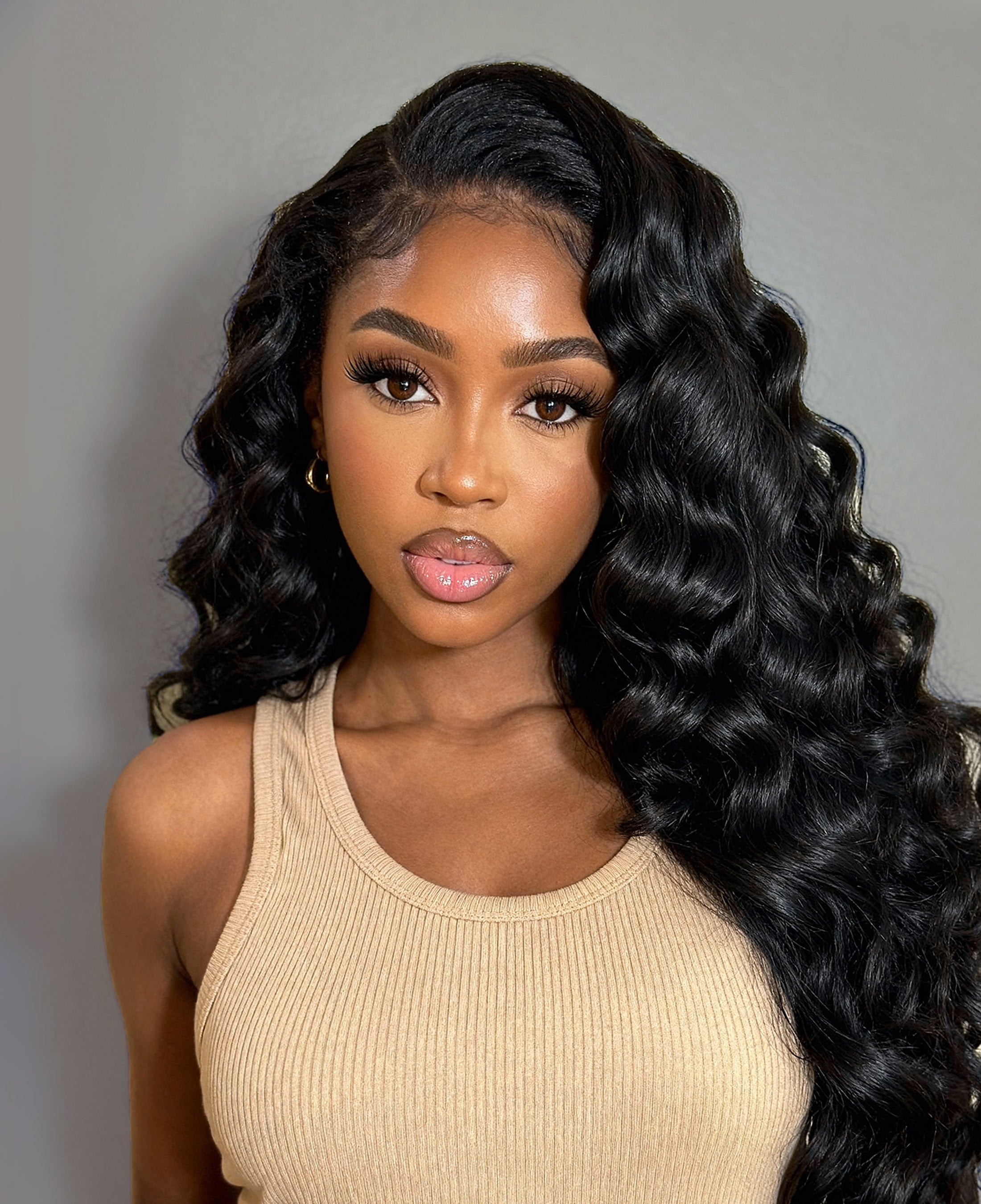 Woman with long, wavy black cambodian hair wearing a beige top against a gray background
