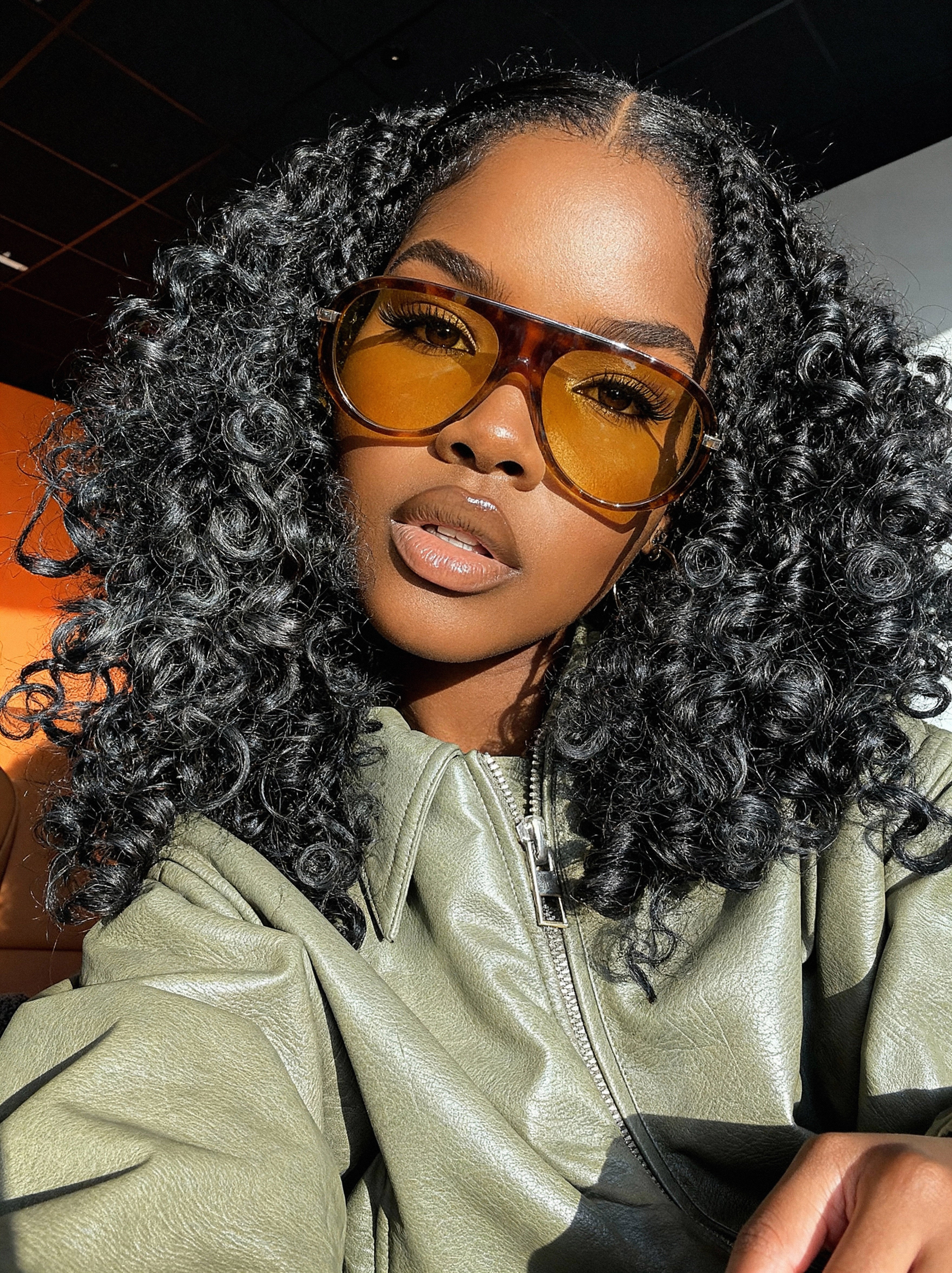 woman wearing a green leather jacket and raw indian curly hair
